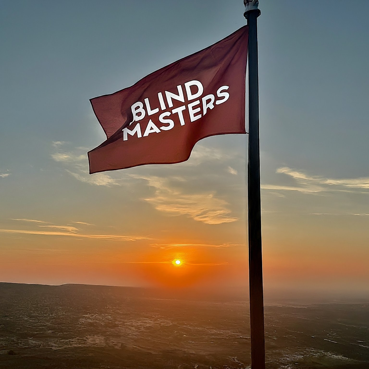 a red flag with the words "blind masters" in white lettering. The flag is waving in the wind, and there is a sunset in the background.